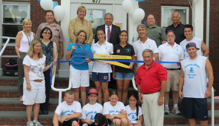 A group of adults and children pose in front of a building, with some holding a large ceremonial key that reads "Town of Hempstead.