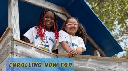 Two children smiling from a wooden play structure at Rolling River Day Camp during summer activities.