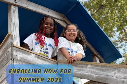 Two children smiling from a wooden play structure at Rolling River Day Camp during summer activities.