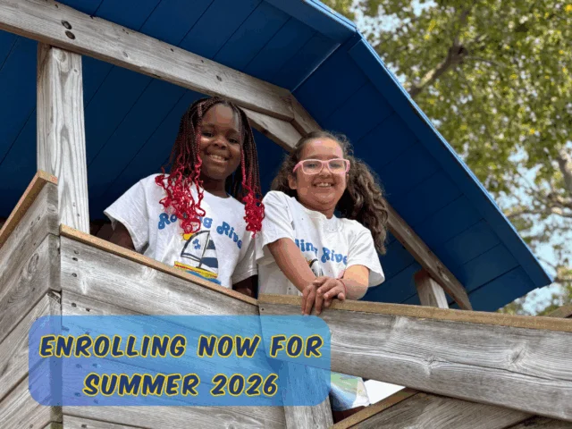 Two children smiling from a wooden play structure at Rolling River Day Camp during summer activities.