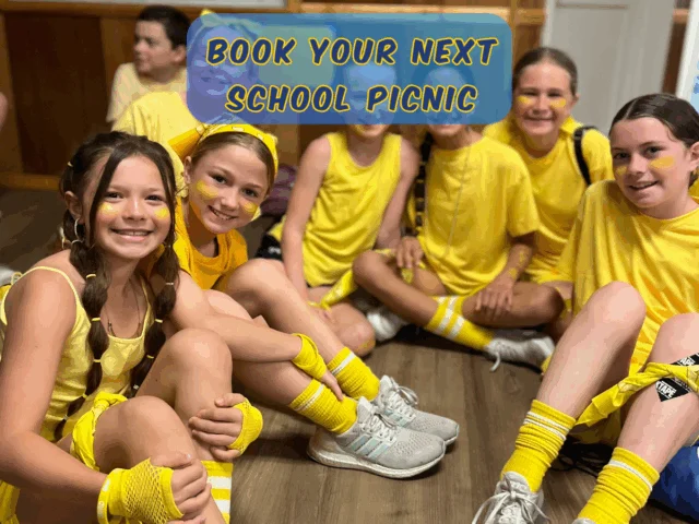 Students wearing yellow shirts sit together smiling during a school graduation picnic at Rolling River Day Camp.