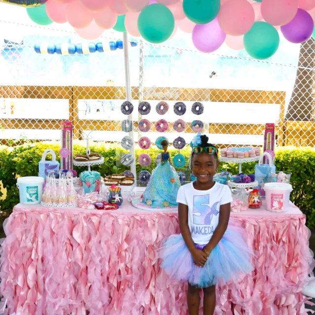A girl wearing a tutu, posing next to her pink birthday party setup.