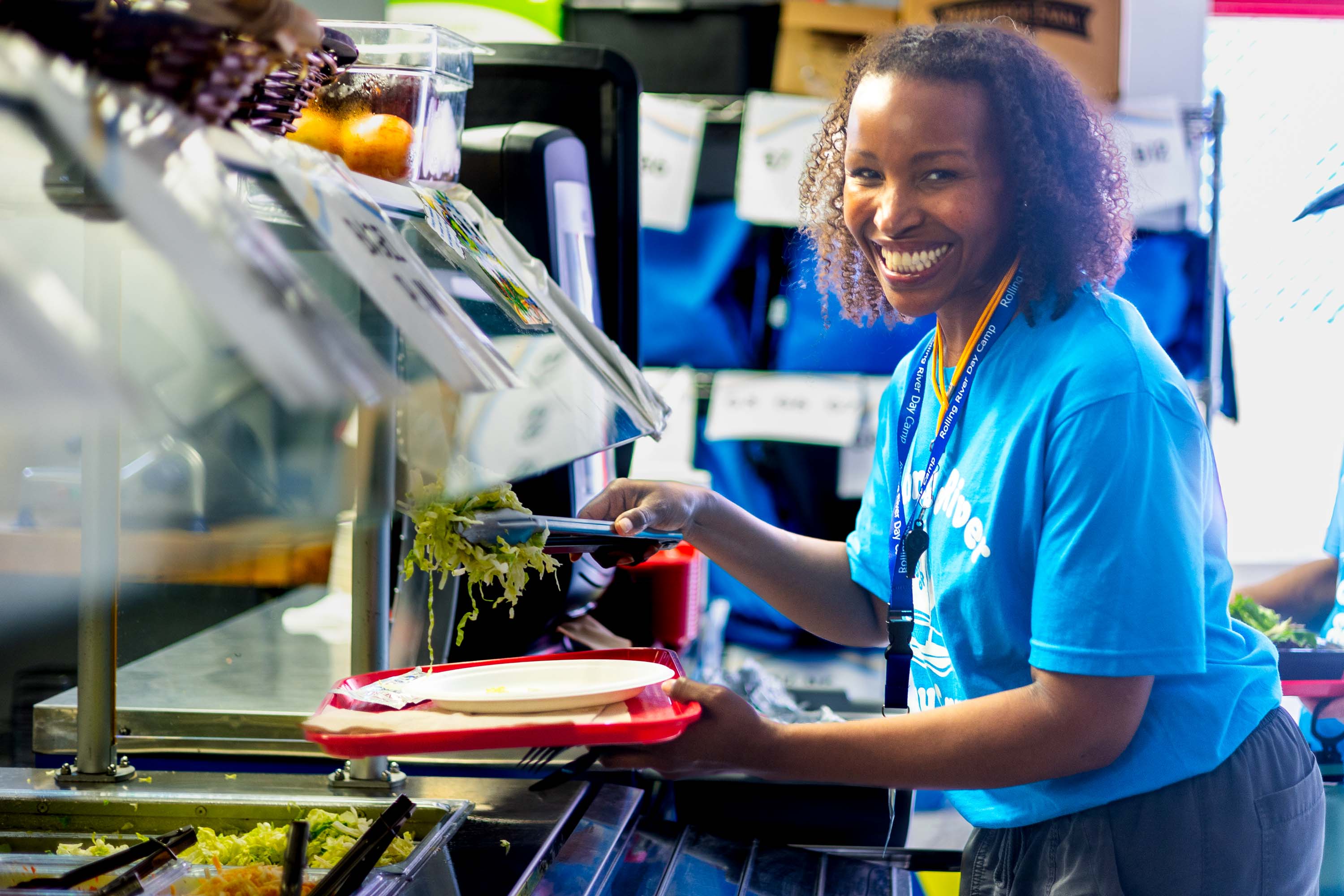 A staff member putting salad on her plate.