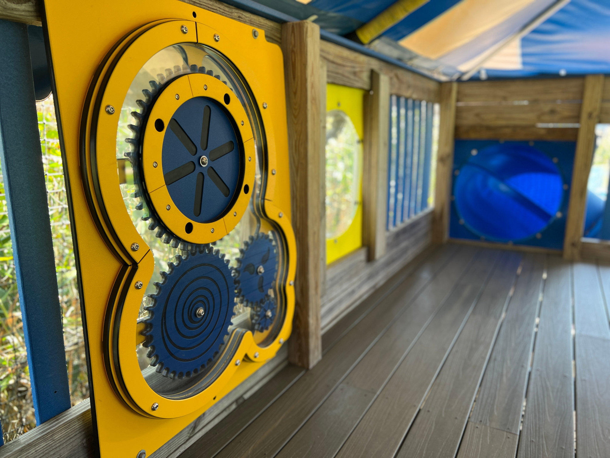 Close-up of an outdoor playground structure featuring large interlocking yellow and black gears mounted on a wooden wall.