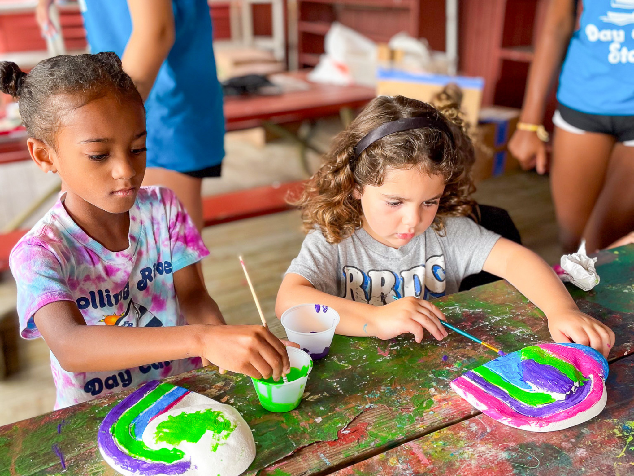 Two campers painting on their pottery work.