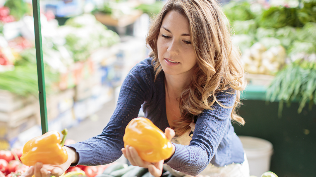 Woman holding a yellow bell pepper in each hand at a farmer's market