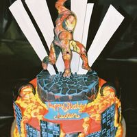 Iron Man Hand painted fondant plaque. Took 4 hrs to paint it (yuck). The molten iron is spilling out of the fondant pots down through the buildings...