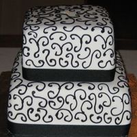 White With Black Scrolls Wedding Cake 6 inch square chocolate cake and an 8 inch square butter cake with buttercream filling. Both cakes are covered with Satin Ice fondant.