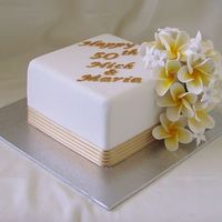 Anniversary Cake 6 inch caramel mud cake covered in white fondx and gumpaste lettering and flowers with fabric ribbon. Frangipani and stephanotis (sp)...