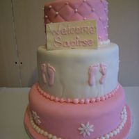 Pink Christening 3 Tiered cake covered in white chocolate fondant. GP booties. White chocolate plaque. RI foot prints. Fondant pearl border.