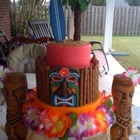 Luau Cake 3-tiered cake iced in buttercream with fondant palm tree and tiki man. Surf board and lei were purchased props. "Bamboo" surround...