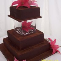 Chocolate Lily Chocolate cake finished with ganache. The top tier is separated with a vase and fresh flowers for decoration.