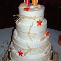At The Beach surf boards for topper made out of fondant and fondant sea shells adadorn the cake. raffia base.