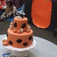 Halloween 2 tiered cake with pumpkins, bats, ghosts, skulls,bones and a witch's head on top.