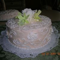 Side View Of Round Cream Colored Cake buttercream icing with flowers (pale green orchids and white fancy flowers) made of gumpaste.