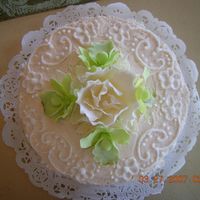 Top View Of Cream Colored Round Cake buttercream icing with pale green orchids and white fancy flowers of gumpaste.