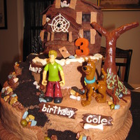 Scooby Doo's Haunted House Haunted house is crispy treats covered in mm fondant. Cake is iced with butter cream icing. Path is crushed oreo's and tree is mm...