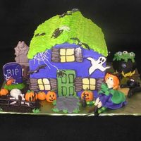 A Witch's House Chocolate cake with ganache filling, iced in buttercream. Decorations are done in chocolate, except for witch, pumpkins, cat, and eyeballs...