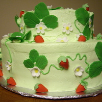 Strawberry Patch Cake Two tier cake with green buttercream icing, fondant strawberries, strawberry flowers, and leaves.