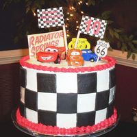 Disney / Pixar Cars Cake Buttercream icing over triple-layer chocolate cake. Fondant checkerboard and Piston Cup; plastic figures and printed flags.
