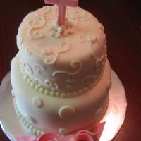 Pink And White Christening two tier round cake covered in mmf. gumpaste bow and cross in pink and dusted with luster dust.
