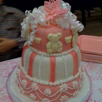 It's A Girl Cake is iced in buttercream and covered in MMF. Bottom layer has royal icing flowers and swags. Middle layer has pink fondant strips and...