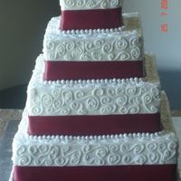 Square 4 Tier Buttercream Scroll With Red Ribbon Cake was white chocolate with white chocolate filling. Buttercream scrolls, fabric ribbon and hand made fondant pearls with silver luster...
