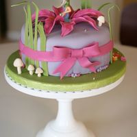 Tinkerbell Cake 9" round cake covered in fondant with plastic Tinkerbell figurine and fondant flower, grass, and mushroom decorations and bow