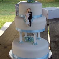 First Wedding Cake White cake covered in fondant. The flowers on top and in the middle are royal icing petunias and the flowers around the columns are blue...