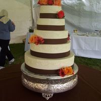 Brown Ribbon This 5-tier wedding cake is covered in buttercream and accented with real brown ribbon and fresh flowers.
