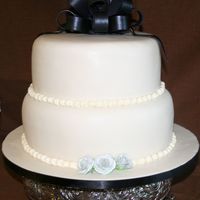 Wedding Cake W/ Bow White chocolate fondant covered, with fondant/gumpaste bow & gumpaste roses. The board is covered in fondant also. Bottom tier is...