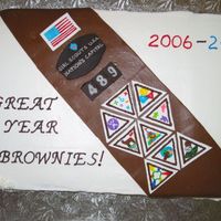 Brownies End Of Year 12x18 sheet cake. Buttercream icing. Tootsie roll "sash". Dark chocolate fondant insigia patches and troop number patches....
