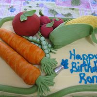 Ron's Birthday Cake Garden theme birthday cake. Fondant covered rice krispie treat veggies. Buttercream hose creates top and bottom cake border, blue piping...