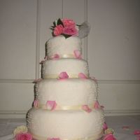 Dotted Ivory Wedding Cake A four tier wedding cake with ivory icing, dots and ribbon. Topped with pink and ivory roses with rose pettles scattered down.
