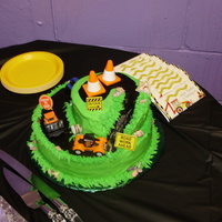 Construction Cake 8" & 10" cake carved for winding road. All iced in buttercream icing and candy rocks. Trucks, cones and signs provided by...