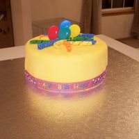 100_1127.jpg Again this is a dummie cake done in yellow fondant, and a happy birthday ribbon, and different colored fondant curls. Balloons are plastic...