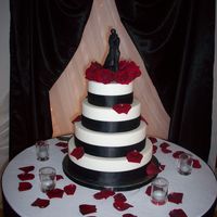 Black, Red And White Wedding Cake 4 tier round wedding cake covered with fondant and accented with black ribbon and roses.
