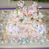 Luau 3 tiers cake with seashell made with white chocolate flavored with pina colada. sugar flowers and coconut flakes all around.