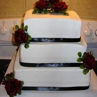 Square Stacked 12", 10", 8" squares. Buttercream icing w/black ribbon trim & silk red roses. Ribbon & Roses selected by the bride...