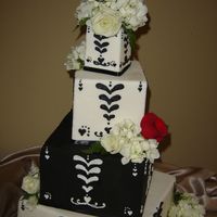 White & Black Square Stacked 3", 6", 9" sqaures styrofoams on top of a 12" square cake, covered in fondant with white and black piping, all edged in...