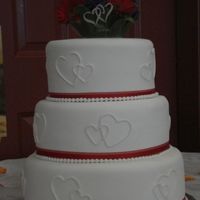 Zello Wedding Fondant covered with linked hearts made with fondant. Real ribbon and fondant pearl border.