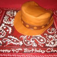 Cowboy Hat And Bandana Cake 12 inch square cake for the base covered with chocolate buttercream with red coloring added to make frosting dark red. Hat covered with MMF...