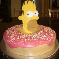 Homer Simpson And His Illustrious Donut! This is a single-tier three-layer chocolate cake decorated with chocolate buttercream frosting. Homer's head is sculpted fondant, and...