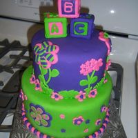Baby Girl Shower Cake Purple, Pink, and Green decorated cake. Baby Block petit four cakes on top