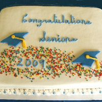 2009Gradresize.jpg All white buttercream background accented with blue and rolled buttercream graduation caps and confetti sprinkles complete this celebration...