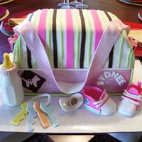 First Diaper Bag Cake White almond and yellow cake covered in fondant. Fondant shoes, keys, and pacifier. Bottle is molded of solid white chocolate
