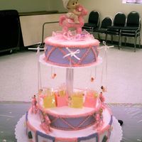 Pink Rocking Horse Carousel 3 tier baby shower cake. Top layer has babies swinging, middle layer is setting on top of the bottom layer. Bottom layer has rocking horses...