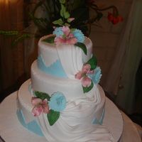 Pink & Blue Covered in fondant. The flowers are also fondant. The fabric work is gumpaste. The color theme for the wedding was pink and blue.