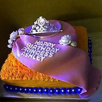 Ashley Princess Cake Orange and blue buttercream with candy pearls. Top tier is covered with pink fondant with luster dust. Tiara is not edible.