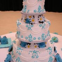 Blue Daisy Cake was iced with whipped frosting, buttercream icing for borders, royal icing daisies. Silk flowers between tiers, on top and around cake...